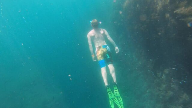 Young caucasian man with a snorkel mask and fins swims freediving underwater. Shooting with an action camera