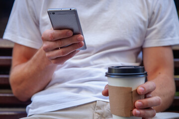 Portrait of young businessman holding  phone and a coffee outdoors. Coffee break, work, overtime work, goal, success concept. Horizontal image.