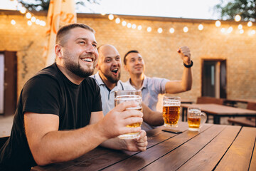 Friends drinking beer together at pub and watching football