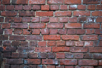 Texture of an old exterior unever brickwork surface made of red bricks. Bricks are aged and weathered with mold, crumbled mortar and numerous cracks.