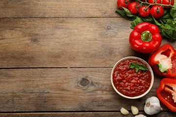 Delicious adjika sauce in bowl and ingredients on wooden table, flat lay. Space for text