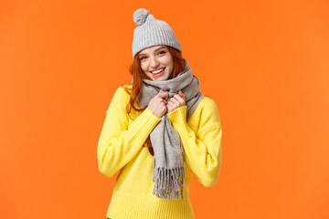 Its getting cold outside. Cute and lovely pretty redhead female wear grey winter hat and scarf, getting warm prepare play snowballs with friends outside during winter holidays, orange background