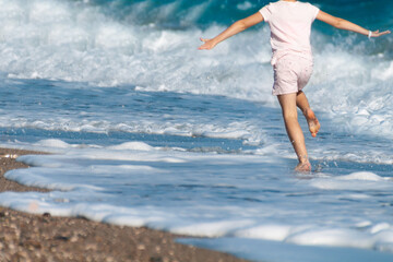 a child runs along the seashore among the waves on a clear day