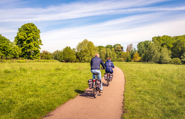 A man and a woman are cycling on a curved bicycle path in a Dutch nature reserve. It is a sunny day...