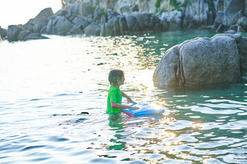 Fototapeta na wymiar Happy child playing in the sea with bodyboard. Child having fun outdoors. Concept of summer vacation and healthy lifestyle