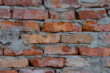 Closeup pfoto of an old brickwork. Texture of an old exterior unever brickwall surface made of red bricks. Bricks are aged and weathered with mold, crumbled mortar and numerous cracks.