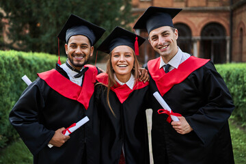 Portrait of three happy smiling graduate friends celebrating graduation in university campus with...