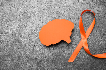 Orange ribbon and paper brain cutout on grey table, flat lay with space for text. Multiple...