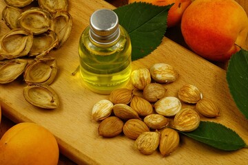 Apricot oil in a bottle, fresh apricots, green leaves and apricot kernels are on a wooden board