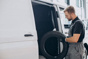 Car mechanic holding new tires by the white van