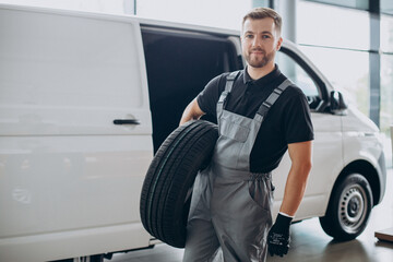 Car mechanic holding new tires by the white van © Petro