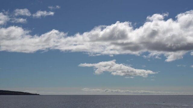 You can see prominent clouds in the sky under a quiet sea. On the left, you can see a parcel of a remote island.