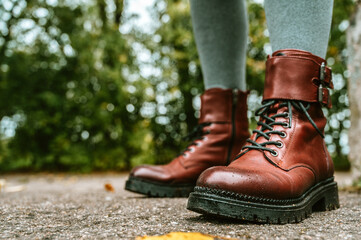 Close-up of legs in burgundy leather shoes. Asphalt with fallen leaves. Autumn fashion for women.
