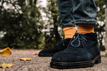 Close-up of legs in blue suede shoes and yellow socks. Asphalt with fallen leaves. Autumn fashion for men.