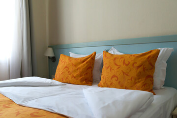 the interior of a small inexpensive hotel room for two persons with double bed. The bed is covered with orange blanket and orange pillows.