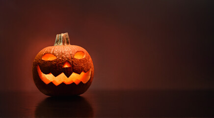 Carved and illuminated halloween pumpkin with dark reddish background front