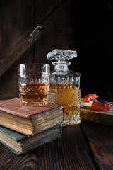Crystal rectangular decanter of high quality whisky and old books on a wooden table with evening warm light atmosphere .
