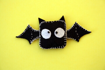 A black bat sewn from felt on a yellow background. A toy for Halloween.