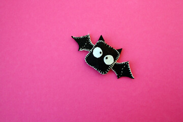 A black bat sewn from felt on a pink background. A toy for Halloween.