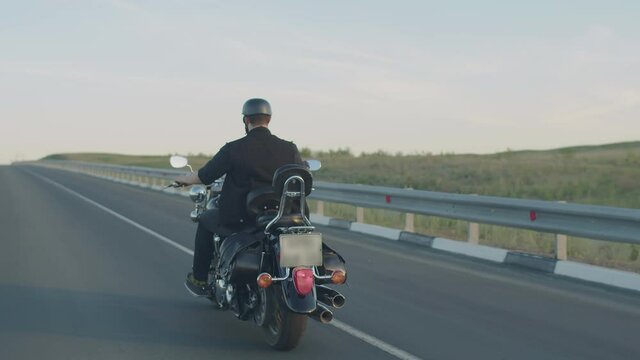 Male biker in helmet rides on highway, back view. Male motorcyclist rushes on motorcycle road, closeup. Concept of speed, masculinity and drive
