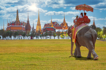 Naklejka na ściany i meble Couple tourists on an elephant ride tour of the grand architecture, a venue now mostly used for ceremonial events. The Buddhist temple of Wat Phra Kaew at the Grand Palace in Bangkok, Thailand