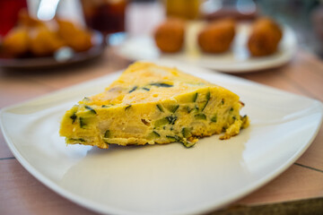 Close up view of an authentic spanish omelette 'Tortilla', made with eggs, fried potato and vegetables, sliced and served on a white plate.