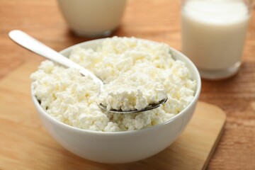 Delicious fresh cottage cheese in bowl on wooden table, closeup