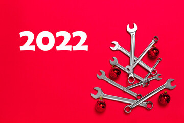 2022 Christmas tree made of wrenches decorated with balls on a red background. Happy New Year banner with tools. Postcard with copy space for greeting text. Industrial holiday concept. Calendar card