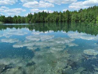 Fototapeta premium The shore of the lake is bright with clear water, in which you can see the marble on the bottom and reflect the sky with clouds, in the mountain park Ruskeala.