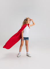 Beautiful caucasian little girl's portrait standing wearing red cape isolated on gray studio background with copyspace for ad