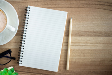 Top view of office desk with pencil, coffee mug, eyeglasses, tree placed on wooden desk get ready for online courses with copy space. You can write and take note of important content in note book.