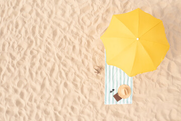 Beach umbrella near towel and other vacationist's stuff on sand, aerial view. Space for text