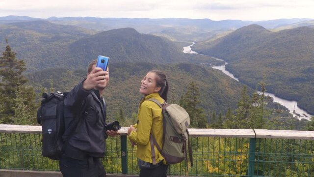 Hiking couple with backpacks in Quebec National Park in Autumn season taking selfie photos in Canada forest travel lifestyle. Tourists looking at view of Jacques Cartier National Park