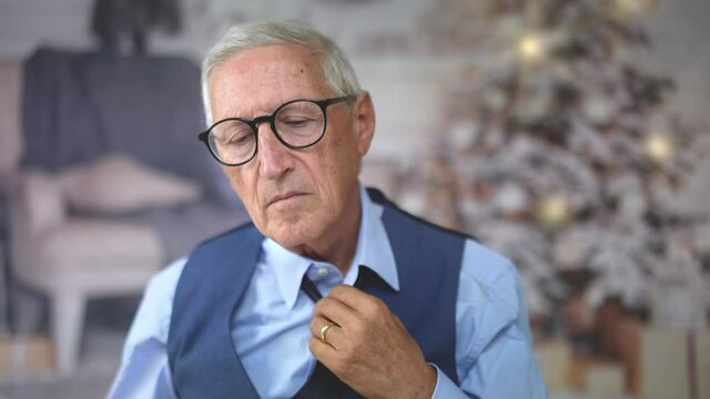 Tired mature businessman, in suit unknots the tie while is working hard, at the office or at home, at Christmas time. Suffering from fatigue. Overwork.
