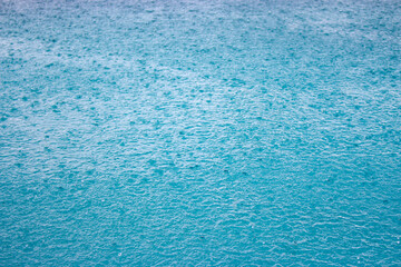 Blue water background with rain drops. Downpour drops on water surface. Ripple on pool surface. Blue shiny agua backround. Rain splash on water. Liquid textured. Water wallpaper.