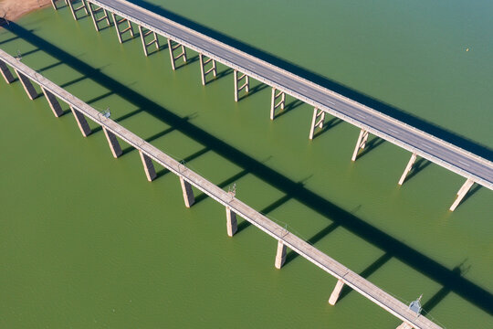 Aerial view of two parallel bridges casting shadows over the water of  large lake