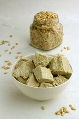 Sunflower halva in a bowl and seeds in a glass jar on light background