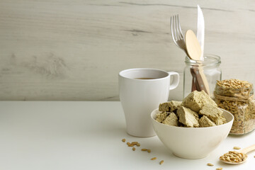 Sunflower halva in a bowl, seeds in a glass jar, cup of tea on light background with copy space
