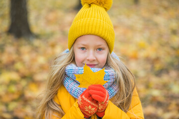 Little blond girl in yellow clothing with yellow leaf, autumn