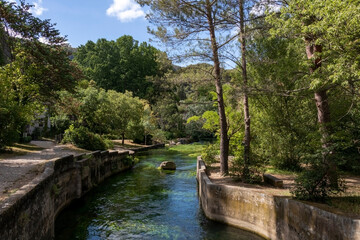Fototapeta na wymiar Fontaine-de-Vaucluse old town with river Sorgue in the foreground, charming medieval village in Vaucluse, Provence, southern France