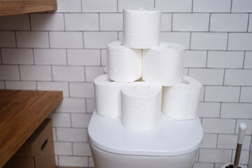 Stack of toilet paper stands on white toilet in bathroom closeup