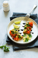 Avocado and salmon sandwiches with balsamic sauce and cilantro on old olive board. Top view
