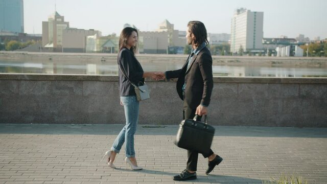 Looping of businesspeople man and woman walking outdoors shaking hands greeting smiling in river embankment on sunny summer day. Business and communication concept.