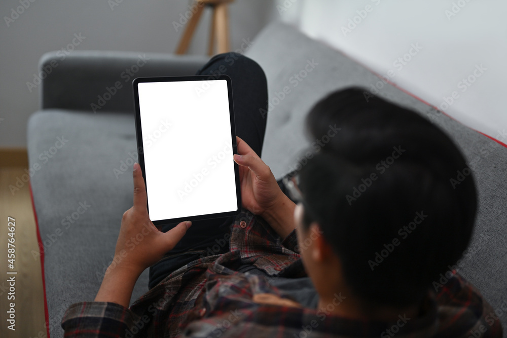 Poster closed up with a man laying on the sofa and using white blank screen digital tablet.