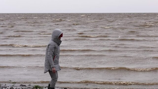 Woman Throwing Stones in Water. Windy Autumn Day at the Shore of Lake Ilmen. Back view