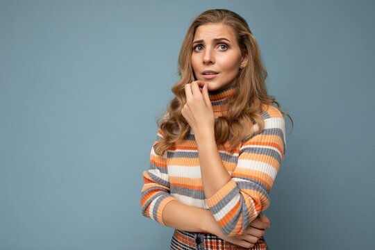 Photo shot portrait of young nice winsome beautiful sad upset thoughtful blonde woman with sincere emotions wearing striped sweater isolated over blue background with free space and having problems