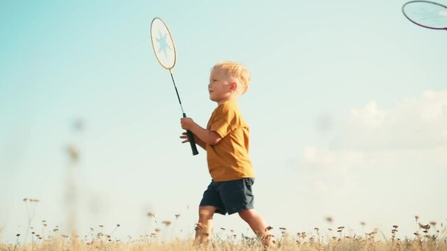 Bottom view of the father giving the badminton racket to his son walking in the other direction in nature