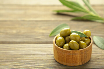 Fresh olives in bowl with leaves on grey background.