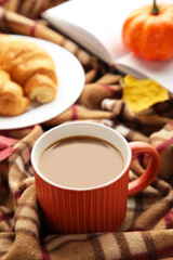Hot coffee with croissant and autumn leaves on plaid - seasonal relax concept. Vertical photo