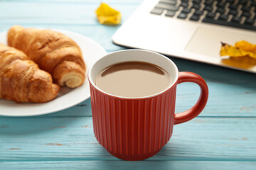 Hot coffee with croissant and autumn leaves on blue - seasonal relax concept.